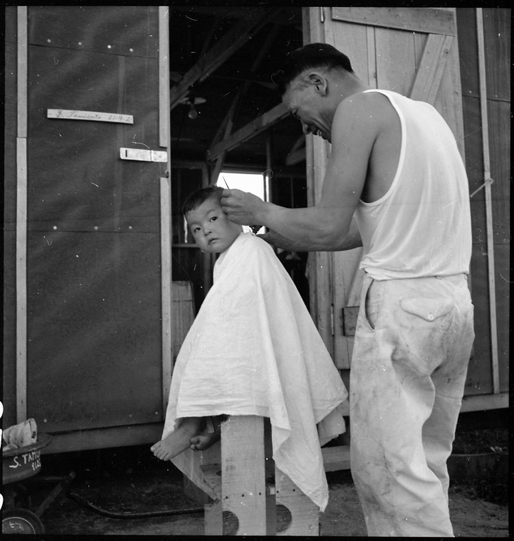 Manzanar Relocation Center, Manzanar, California. Little evacuee of Japanese ancestry gets a haircut.