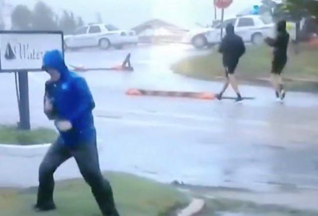 Hilarious fake news: Weather Channel reporter fakes hurricane-force winds while two guys casually stroll down the street behind him, wearing shorts